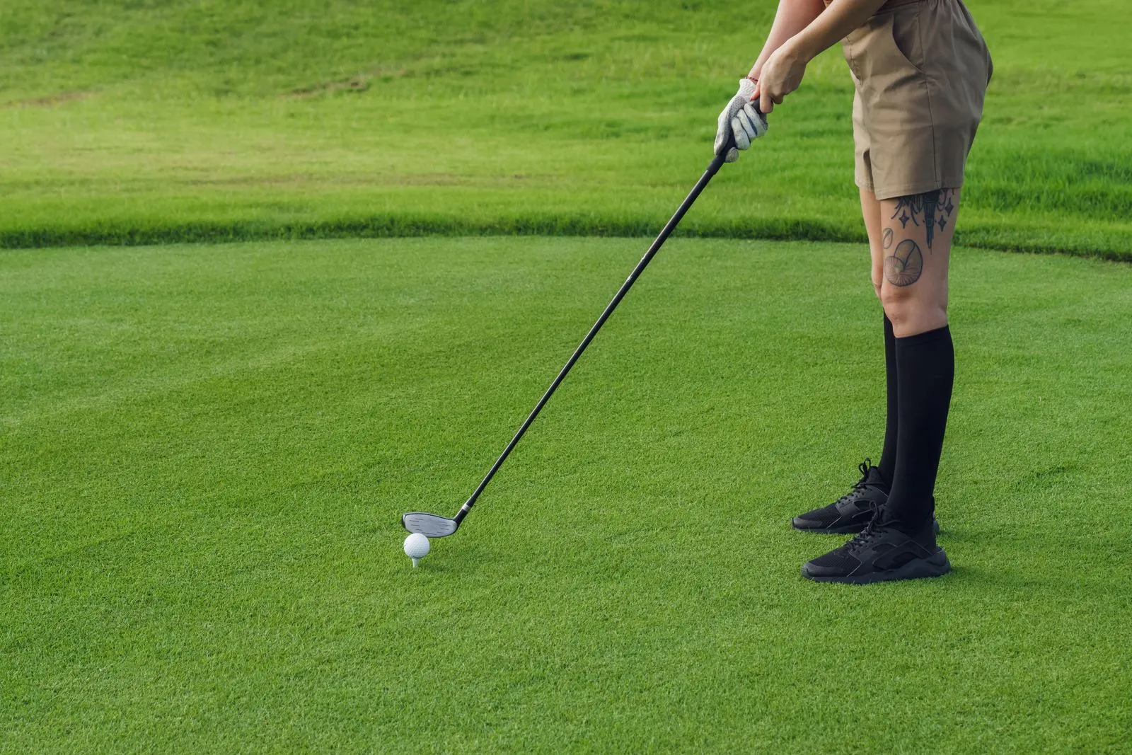 A golfer with tattoos prepares to putt on a lush golf course green.